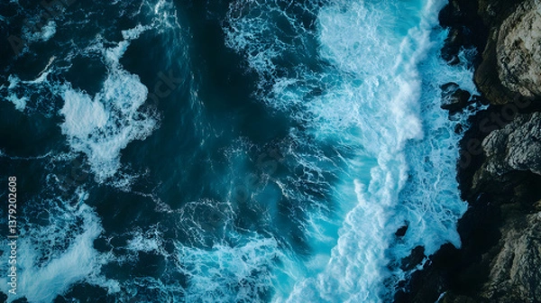 Fototapeta Aerial Top-Down View of Ocean Waves Crashing Against Rugged Cliffs with Dramatic Contrast