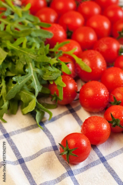 Fototapeta Red ripe cherry tomatoes and fresh spicy rocket salad on white checked towel, focus on foreground