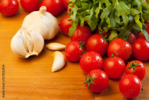 Fototapeta Tomatoes, garlic and rucola on wooden table, focus on foreground