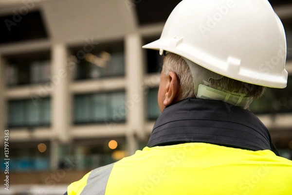 Fototapeta Construction worker / building inspector surveying a tall building.