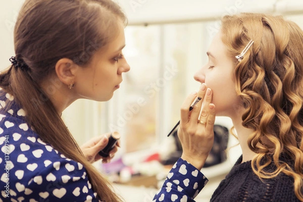 Fototapeta Brunette make up artist woman applying make up for a blonde bride in her wedding day, for a date