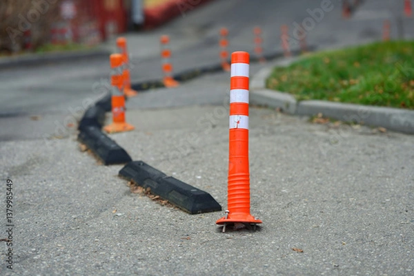 Fototapeta Damaged safety delineator with torn out fastening. Broken road infrastructure, plastic traffic cone. Orange traffic cones with reflective stripes guide vehicles along paved road. Selective focus