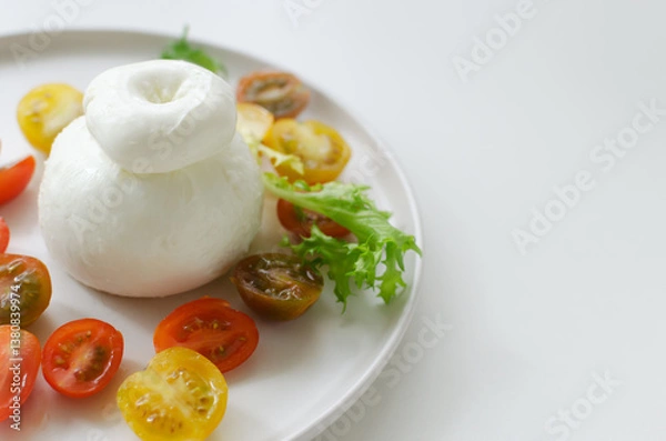 Fototapeta Buratta on a gray plate with cherry tomatoes and herbs on a white table. Traditional Italian food concept. Horizontal orientation. Selective focus. Copy space