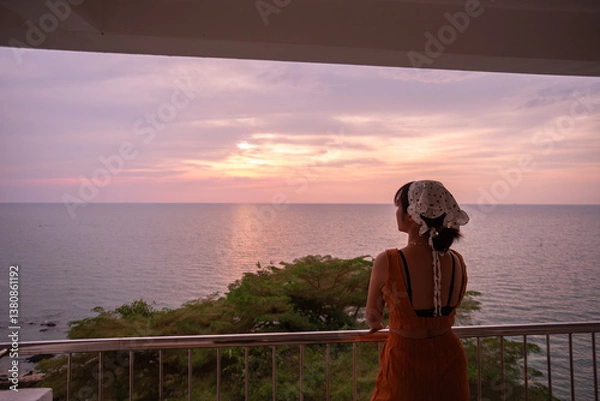 Fototapeta Beautiful Thai woman enjoys the view from the balcony of a beach resort during sunset. Beautiful tourist attraction on Koh Sichang, Chonburi Province, Thailand.