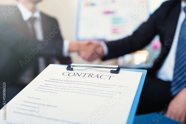 Fototapeta business contract on background of two employees handshaking