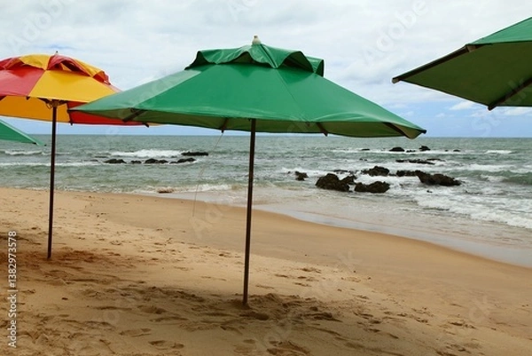 Obraz Vacations on tropical beach. Green parasol on the empty beach sand waiting for tourists, waves breaking on waters edge, splash and white foam. Coqueiros beach, near Joao Pessoa city, Brazil