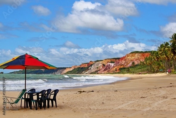 Obraz Beach near Joao Pessoa city, Paraiba state, northeast of Brazil. Parasol and chairs on the empty beach, waves crashing on the water's edge and multi-colored hills