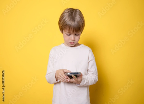 Obraz Little blond child boy using smarphone standing isolated over yellow background.