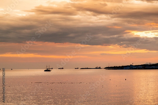 Obraz A beautiful sunset over the ocean with a boat in the water. The sky is filled with clouds and the water is calm