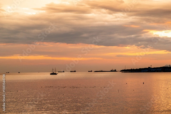 Obraz A beautiful sunset over the ocean with a boat in the water. The sky is filled with clouds and the water is calm