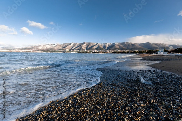 Obraz A rocky beach with a body of water in the background. The water is calm and the sky is clear