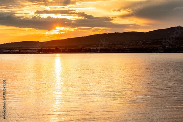Obraz The sun is setting over the water, creating a beautiful orange and pink sky. The water is calm and still, reflecting the colors of the sky. The scene is peaceful and serene