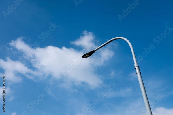 Fototapeta Modern street lamp against a bright blue sky with scattered white clouds. Daytime view.