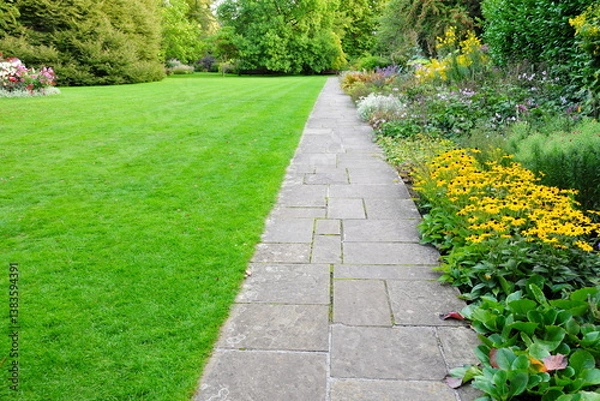 Fototapeta Stone paved path in a beautiful garden with a grass lawn and colourful flowers