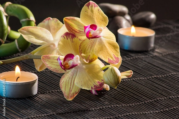 Fototapeta Gelbe Orchideen auf einer Bambusmatte mit Kerzen und schwarzen Steinen