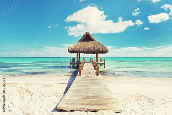 Obraz Tropical white sandy beach. Palm leaf roofed wooden pier with gazebo on the beach. Cross processed. Instagram filter. Punta Cana, Dominican Republic. Instagram filter