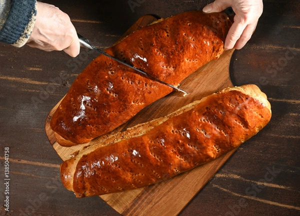 Obraz Freshly baked bread being sliced on a wooden board in a cozy kitchen setting during the afternoon
