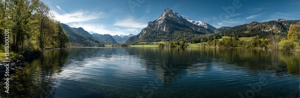 Obraz Panoramic photo of Lake. The lake is clear and calm, reflecting the surrounding mountains and trees in its surface. In front of it stands Mount Hood with snow-capped peaks against a blue sky backgroun