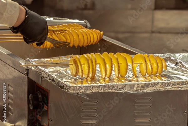 Obraz Raw preparation of tornado potatoes or spiral chips on the background of the hands of a cook with tongs. Street food