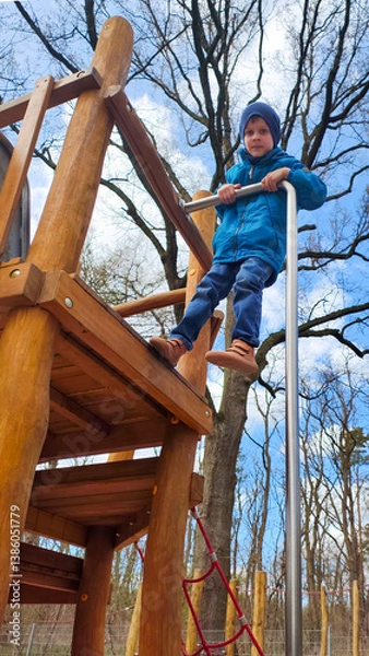 Fototapeta Young boy climbing wooden playground structure, building confidence and strength, active outdoor play, motor skill development for children