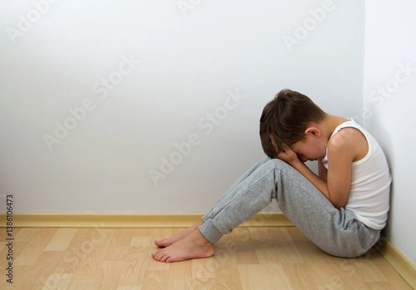 Fototapeta Boy crying with his head down and sitting sad scared on the floor in the corner and hugs his knees. Concept domestic violence and child abuse.