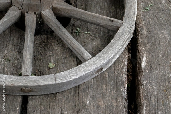 Obraz Fragment of a wooden wheel. A wooden wheel from an ancient cart lies on boards. View of a fragment of ancient technology for making a wheel from natural materials.