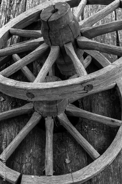 Obraz Fragment of a wooden wheel. A wooden wheel from an ancient cart lies on boards. View of a fragment of ancient technology for making a wheel from natural materials.