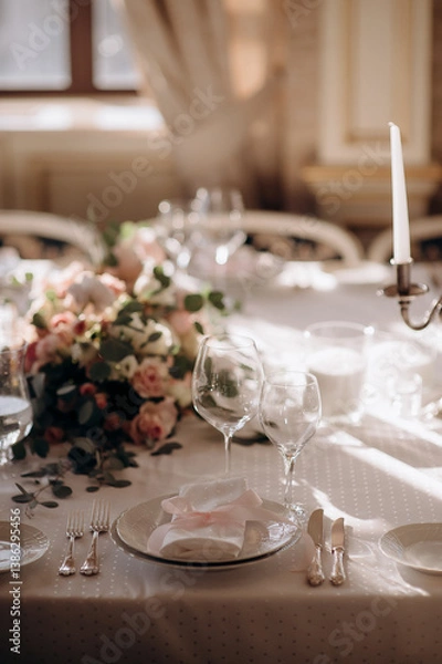 Fototapeta Elegant wedding table setting with a white tablecloth, pink napkins, simple floral centerpiece, and tall white candle in a silver holder