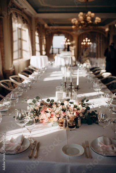 Fototapeta Elegant indoor wedding table setting with a white tablecloth, pink napkins, simple floral centerpiece, and tall silver candlesticks