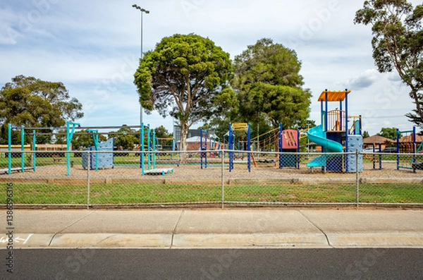Fototapeta A fenced suburban playground features climbing structures, slides, and monkey bars in Australia. Outdoor play area offers a safe and inviting space for children to enjoy recreational activities