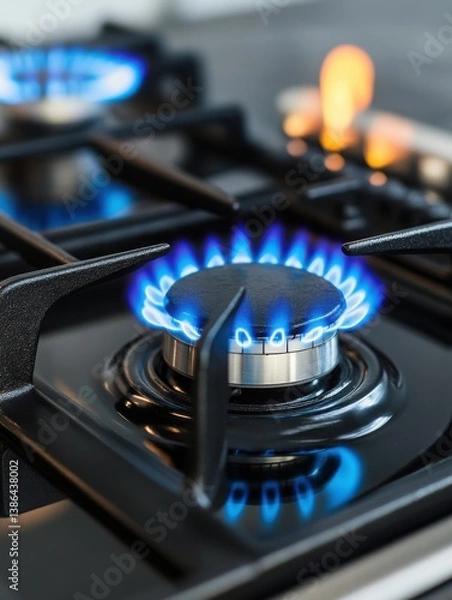 Fototapeta Close-up of a gas stove burner with a blue flame in a modern kitchen.