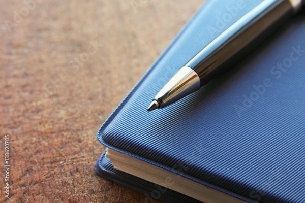 Fototapeta blue notebook and ball pen on an old  wooden background, close up view with copy space.