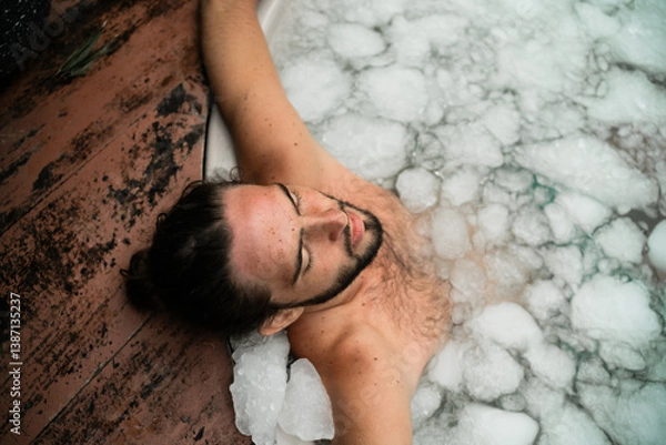 Obraz Man takes an ice bath outdoors in a lush tropical setting. Cold immersion for mental strength, discipline, and physical recovery