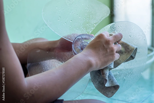 Fototapeta A man is cleaning a fan, including cleaning the propeller, the engine (and providing lubricants), and cleaning the fan guard grill
