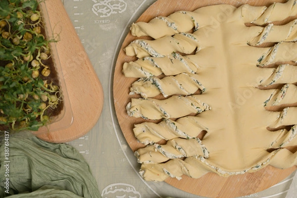 Obraz Top view close up twisted dough strips on wooden board. Green towel, microgreens sprouts on kitchen table. Home cooking baking puffs