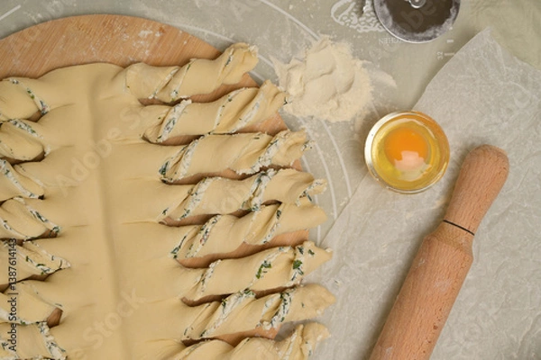 Obraz Top view close up twisted dough strips on wooden board. Cutter, egg, rolling pin on kitchen table. Home cooking baking puffs
