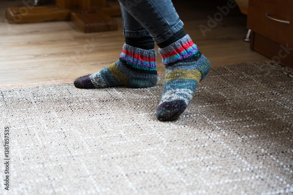 Fototapeta The feet of a girl in wool socks and jeans are standing on the carpet
