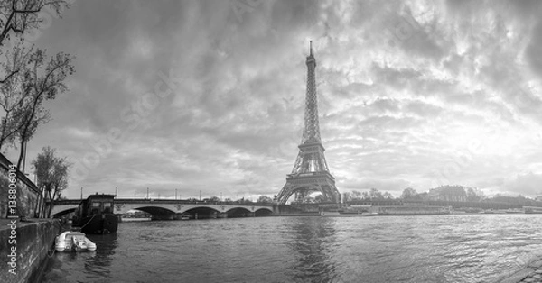 Fototapeta Beautiful panoramic view of the Eiffel Tower and Jena bridge from the river Seine embankment. Dramatic cloudscape. Traditional sitycape in backlit morning sunbeam. BW photography. Paris, France.