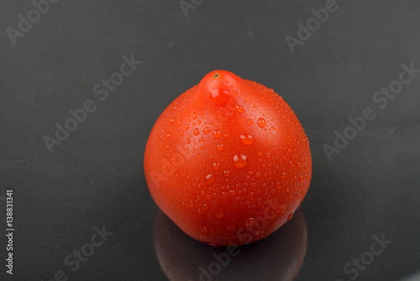 Obraz Single red tomato with drops isolated on black background. Juicy organic cherry perfect for salads, soups, sandwiches or healthy snack.