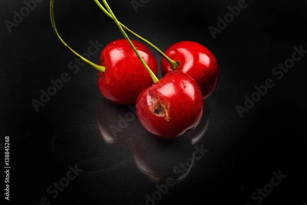 Obraz Two red cherries and one broken against reflective black background. Selective focus. Lights and shadows