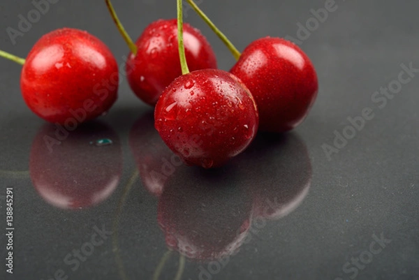 Obraz Three red wet cherries against reflective black background in studio. Selective focus. Lights and shadows
