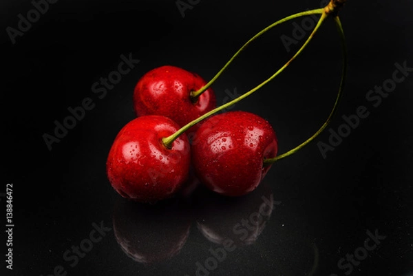 Obraz Three red cherries with water drops against reflective black background. Selective focus. Lights and shadows. Healthy and sweet food