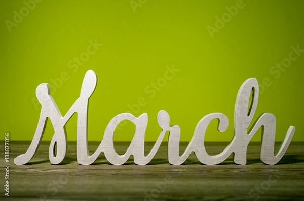 Fototapeta Close Up March word carved out of wood on green background. Spring beginning concept