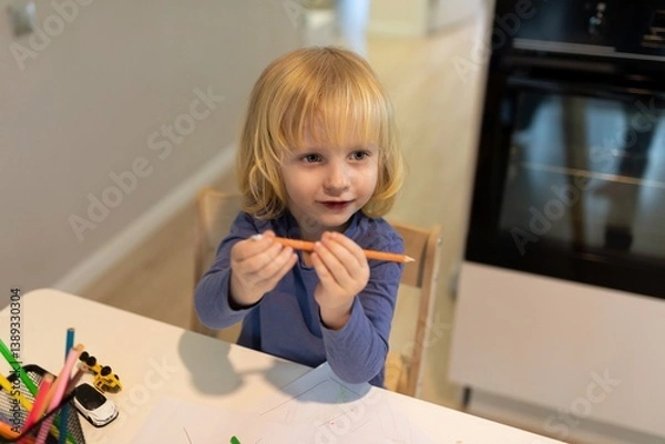 Obraz Young child enjoys creative time with colored pencils at a modern kitchen table in a cozy home setting