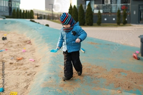 Obraz Child explores sandbox in urban park on a cool afternoon, enjoying outdoor playtime in winter attire
