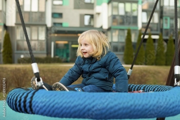 Fototapeta Child enjoys swinging on a large tire swing in a modern park setting during the afternoon