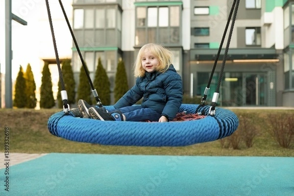 Fototapeta Child enjoys swinging on a circular swing in a modern playground during a sunny afternoon