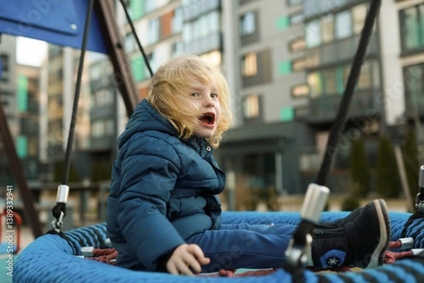 Obraz Child joyfully playing on a swing at a modern urban playground in the early afternoon