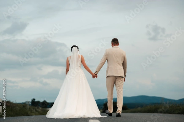 Fototapeta Together on the road ahead, hand in hand. Standing still for a moment, yet moving toward forever — their journey begins on this path, paved with love and endless promise