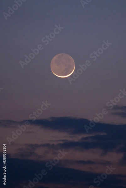 Fototapeta A stunning young moon illuminating the sky above the clouds